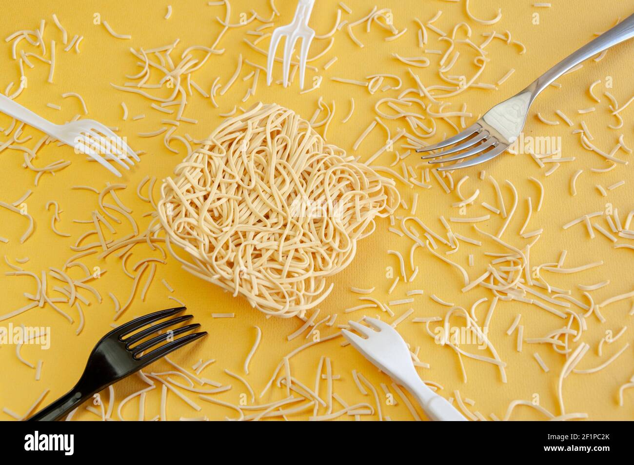 Range of disposable plastic forks around egg instant noodle scattered on yellow background. Stock Photo