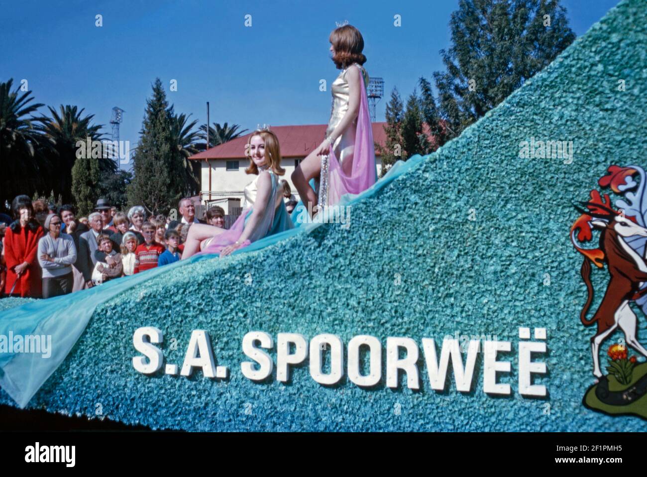 Parade float promoting South African Railways (Spoorweë in Afrikaans), during the apartheid era, Durban, South Africa, 1966. There are two beauty queens wearing crowns on the float. It’s very much a white audience viewing this event. This image is from an old amateur 35mm Kodak colour transparency. Stock Photo