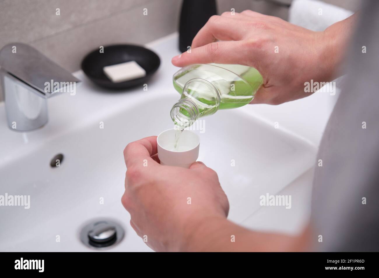 Man pouring green mouthwash from bottle into cap in bathroom. Teeth