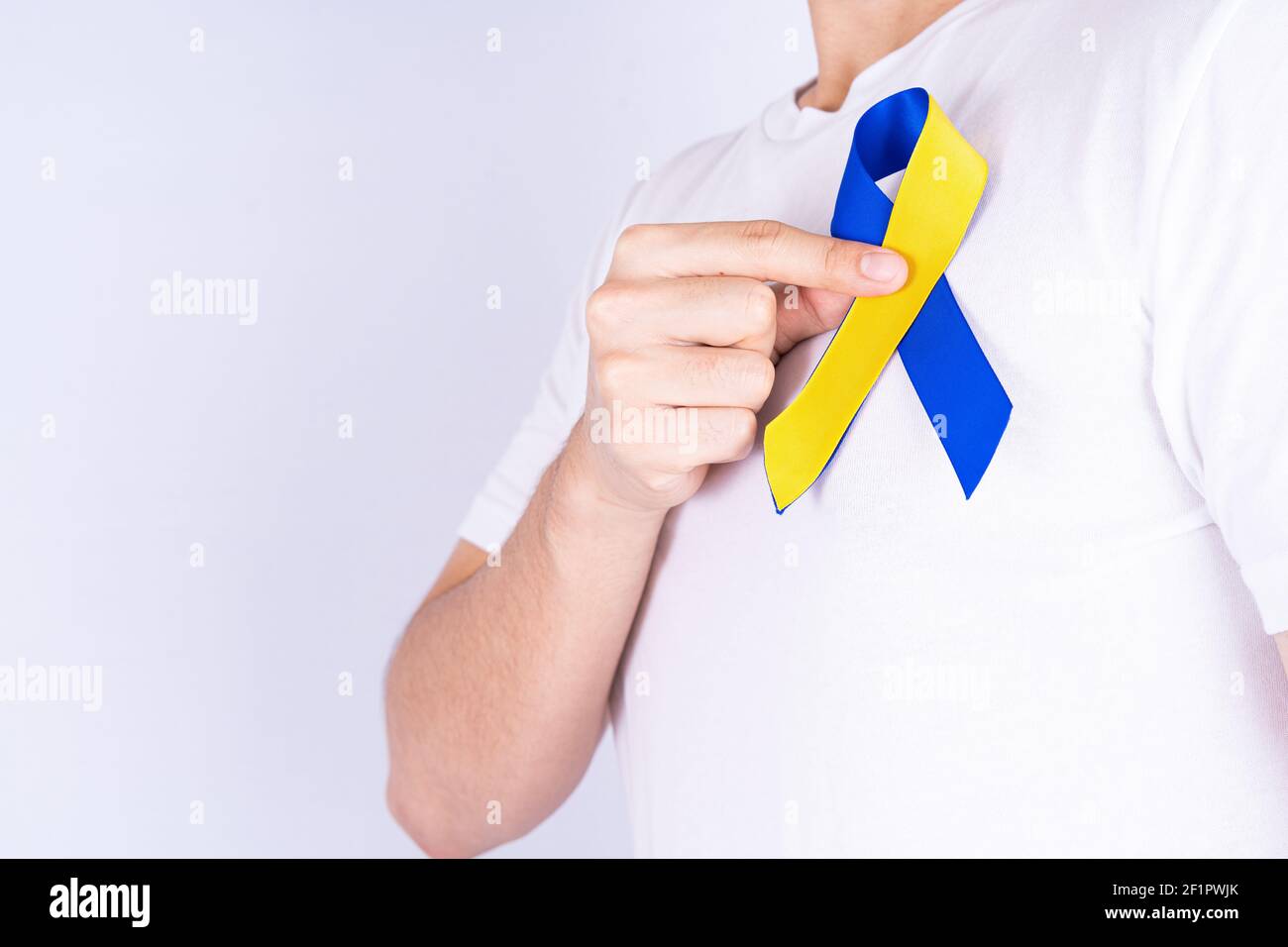 Down syndrome day, hands holding blue yellow ribbon awareness on chest ...