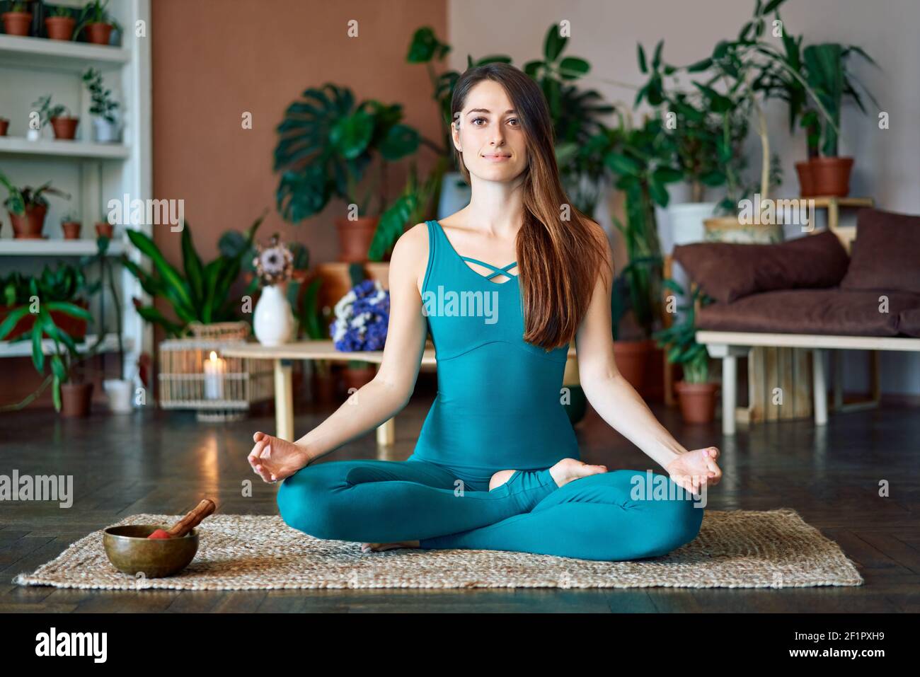Young attractive woman practicing yoga sitting in lotus pose and meditating at home. Ardha Padmasana exercise. balance and recreation concept Stock Photo