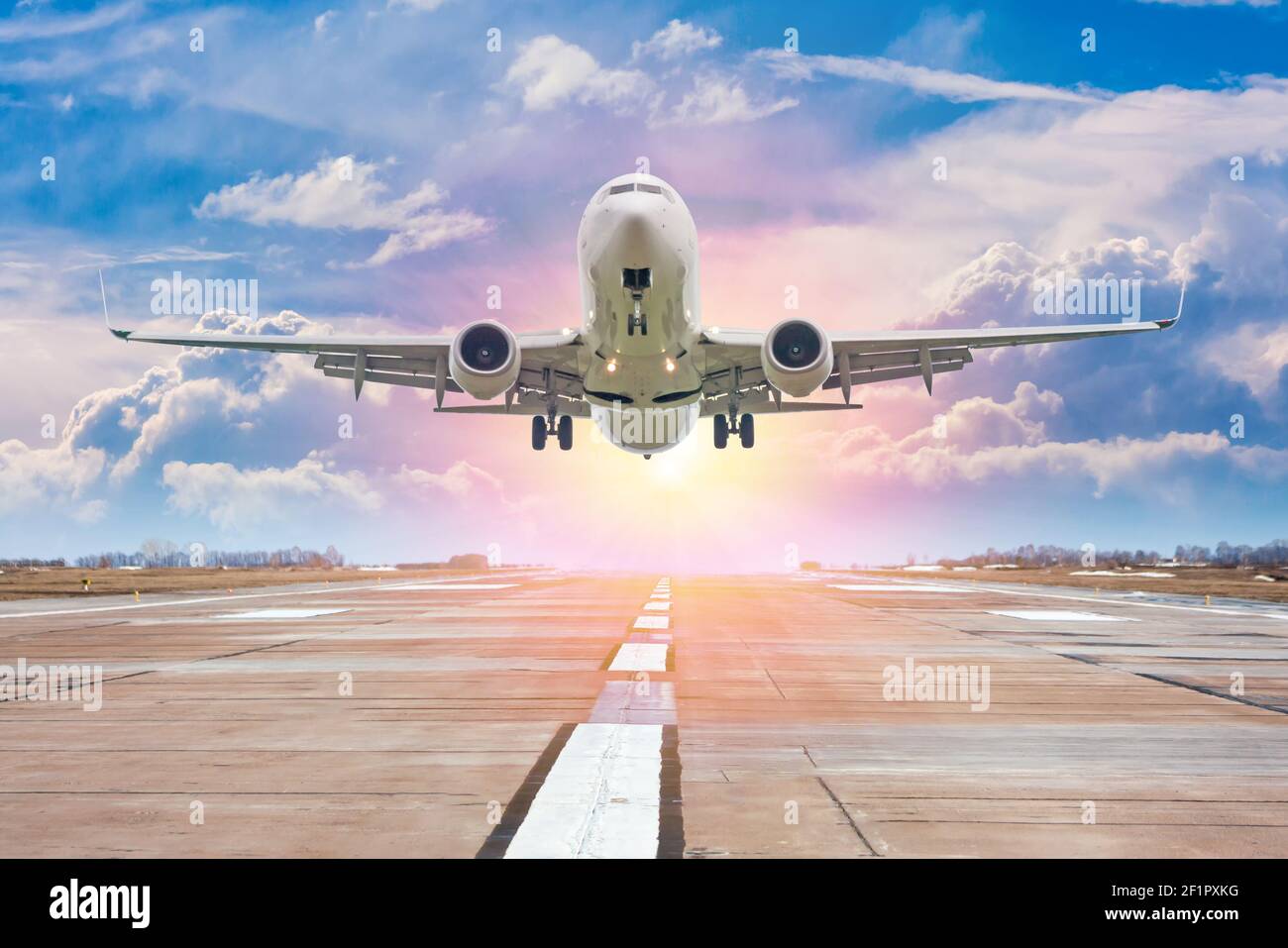 White passenger airplane take off from airport runway against the backdrop of a picturesque evening sky with sun rays Stock Photo
