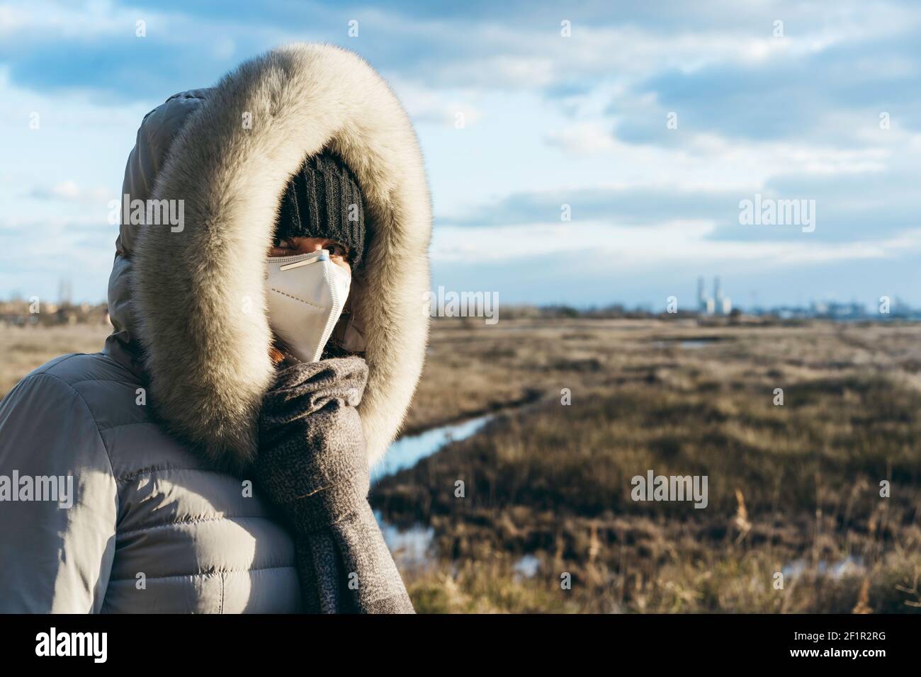 Worried woman wearing a protective face mask and winter clothes with  grassland wilderness and factories on the background - Activism and  environmenta Stock Photo - Alamy