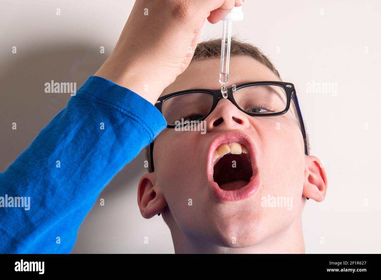 Child with glasses drips medicine from pipette into mouth Stock Photo