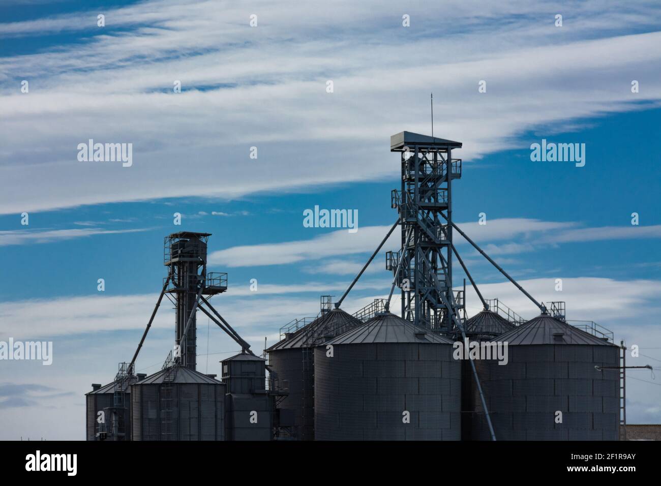 Set of grain storage silos of various sizes and blue sky with clouds
