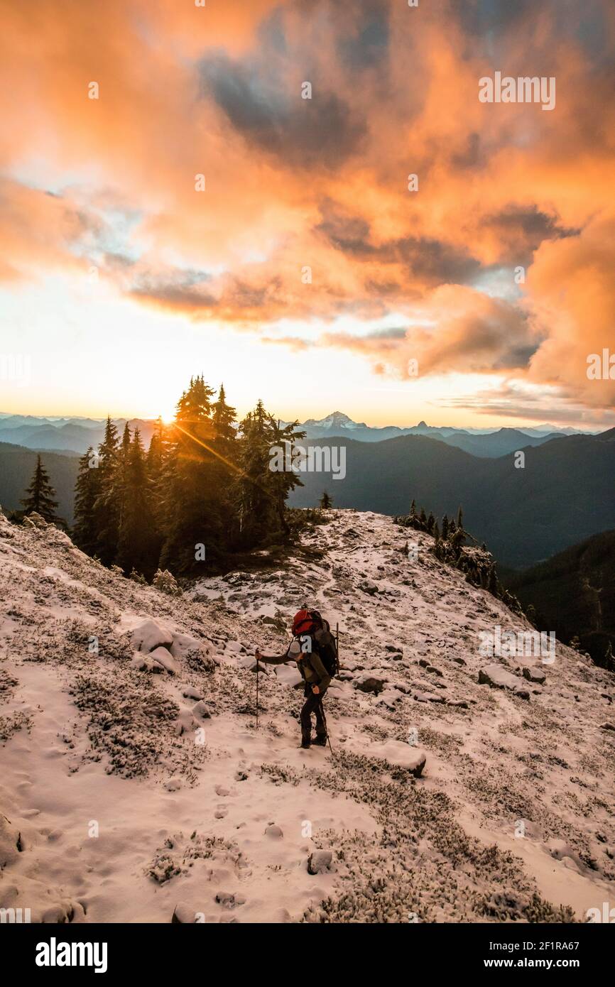 Man hiking on mountain ridge with sunset, scenic view behind. Stock Photo