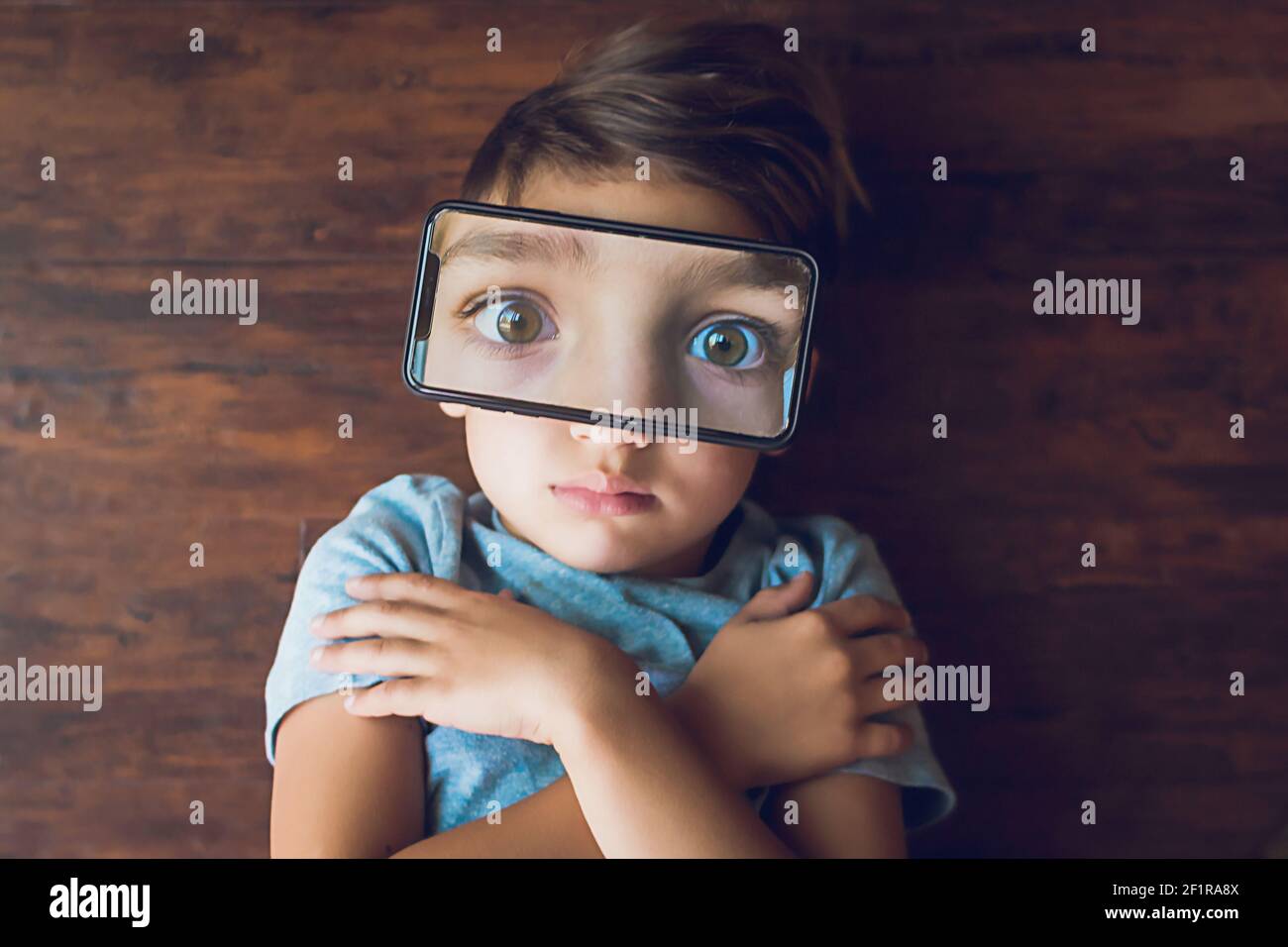 Boy laying on the ground with a phone photo of his eyes on top of face Stock Photo