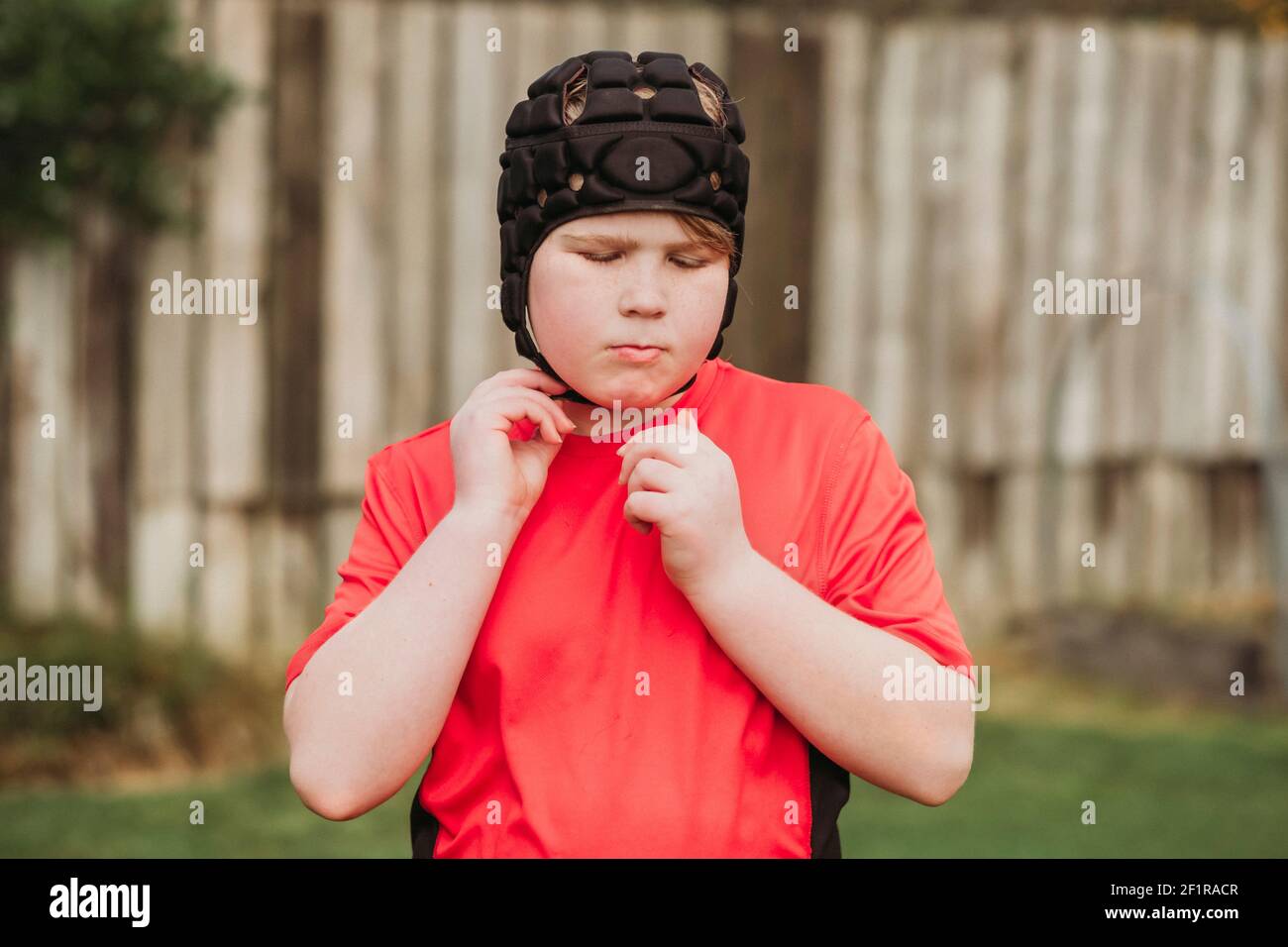 Boy putting on rugby protection head gear in backyard Stock Photo
