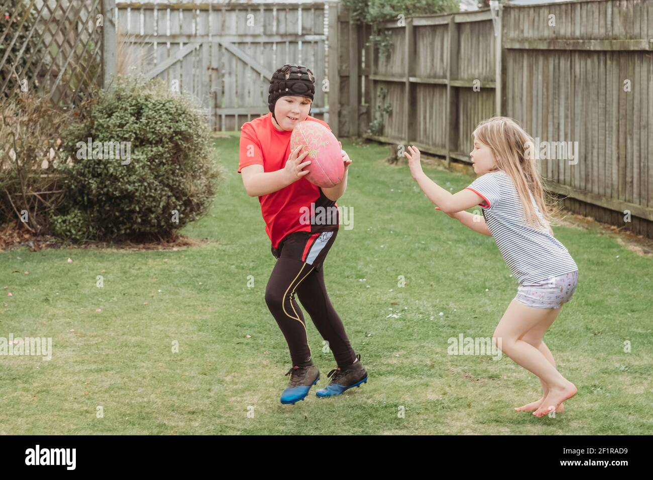 Young brother and sister playing with rugby ball in backyard Stock Photo