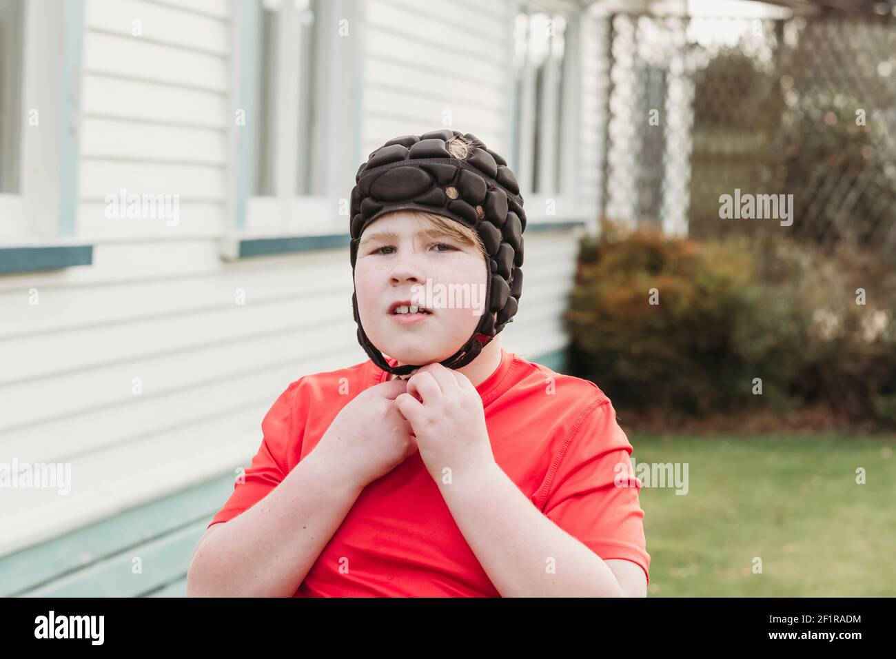 Boy adjusting protective rugby head gear in backyard Stock Photo