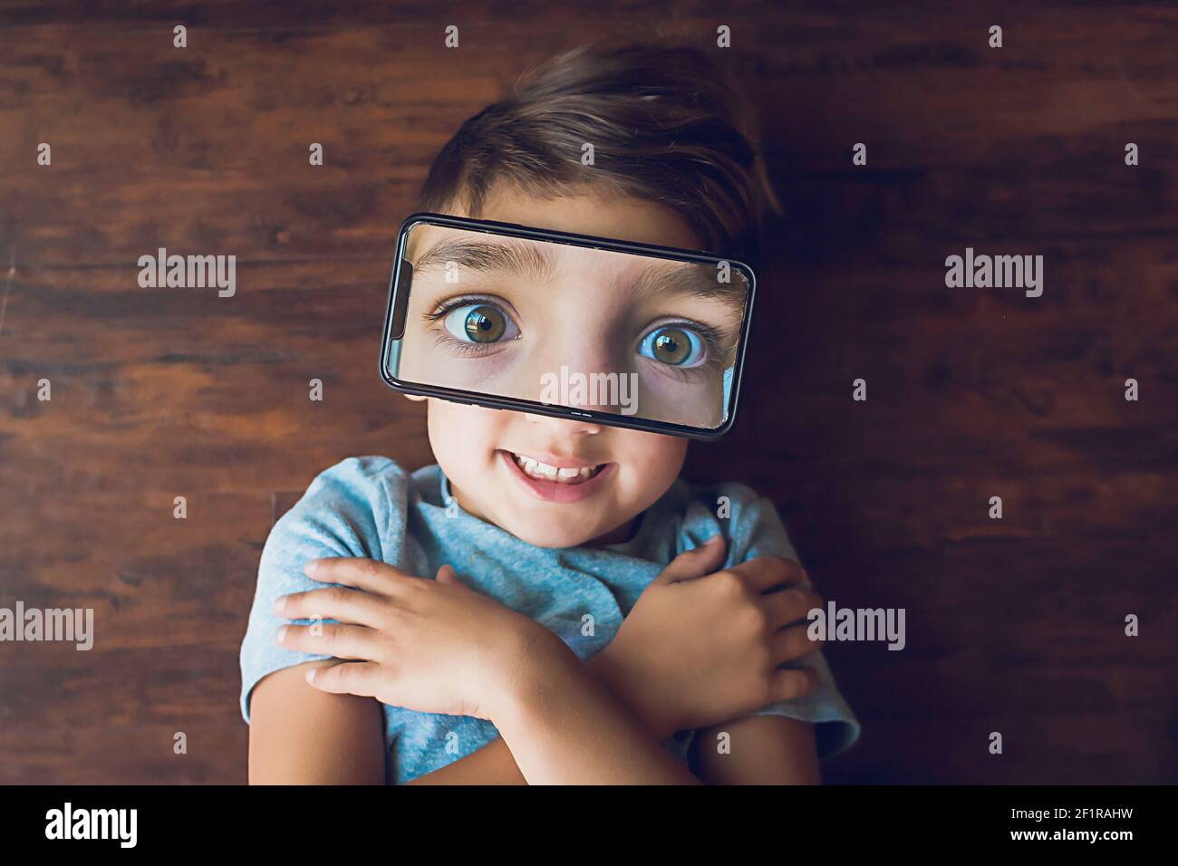 Boy laying on the ground with a phone photo of his eyes on top of face Stock Photo
