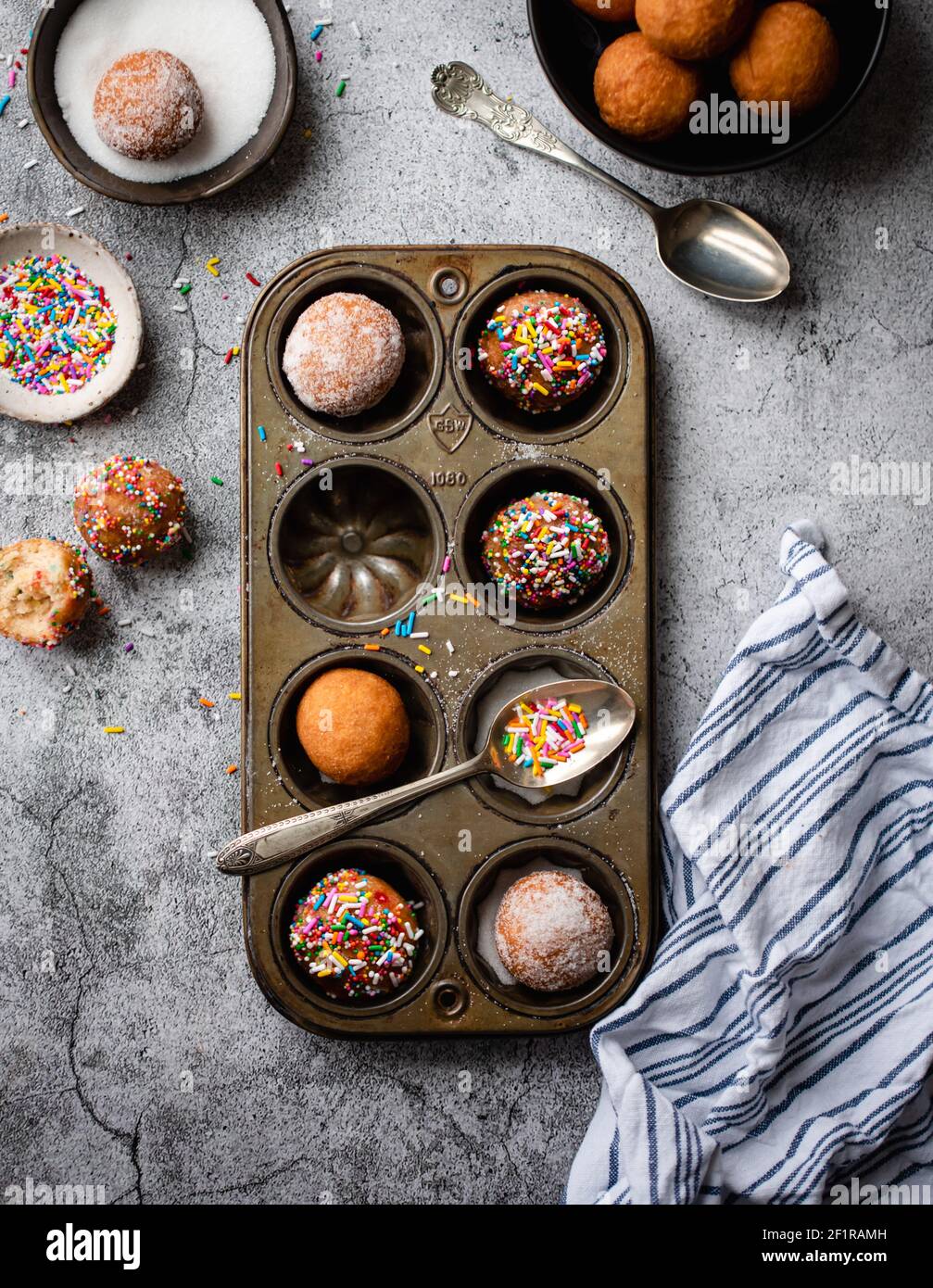 Overhead of donut holes covered in sugar and sprinkles in baking tin. Stock Photo