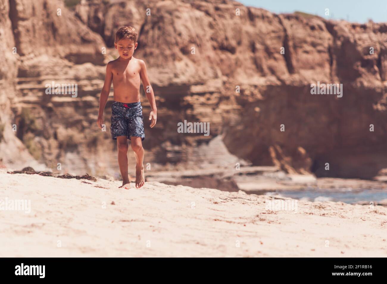 School age boy walking alone on a beach with cliffs in the background