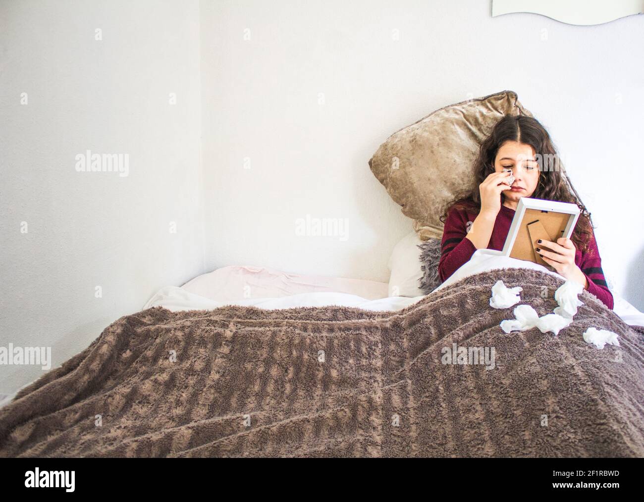 young woman lying crying with photograph and handkerchiefs in bed Stock Photo