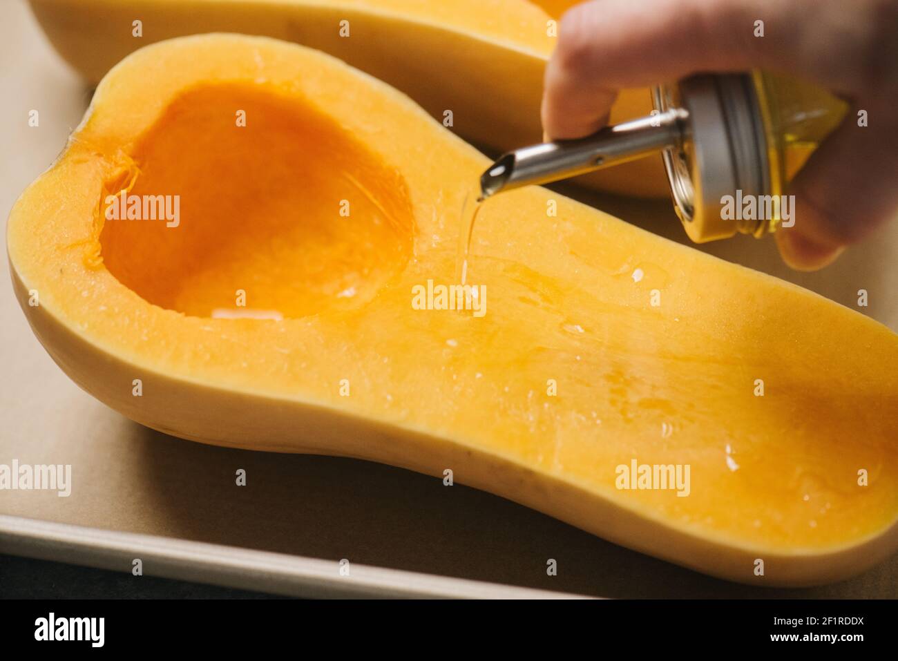 Pouring olive oil over a halved butternut squash Stock Photo