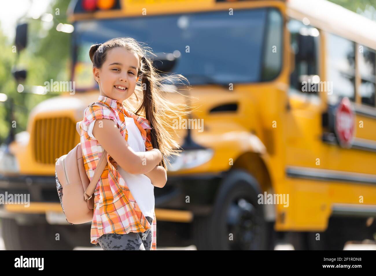Little girl standing by a big school bus door with her backpack Stock