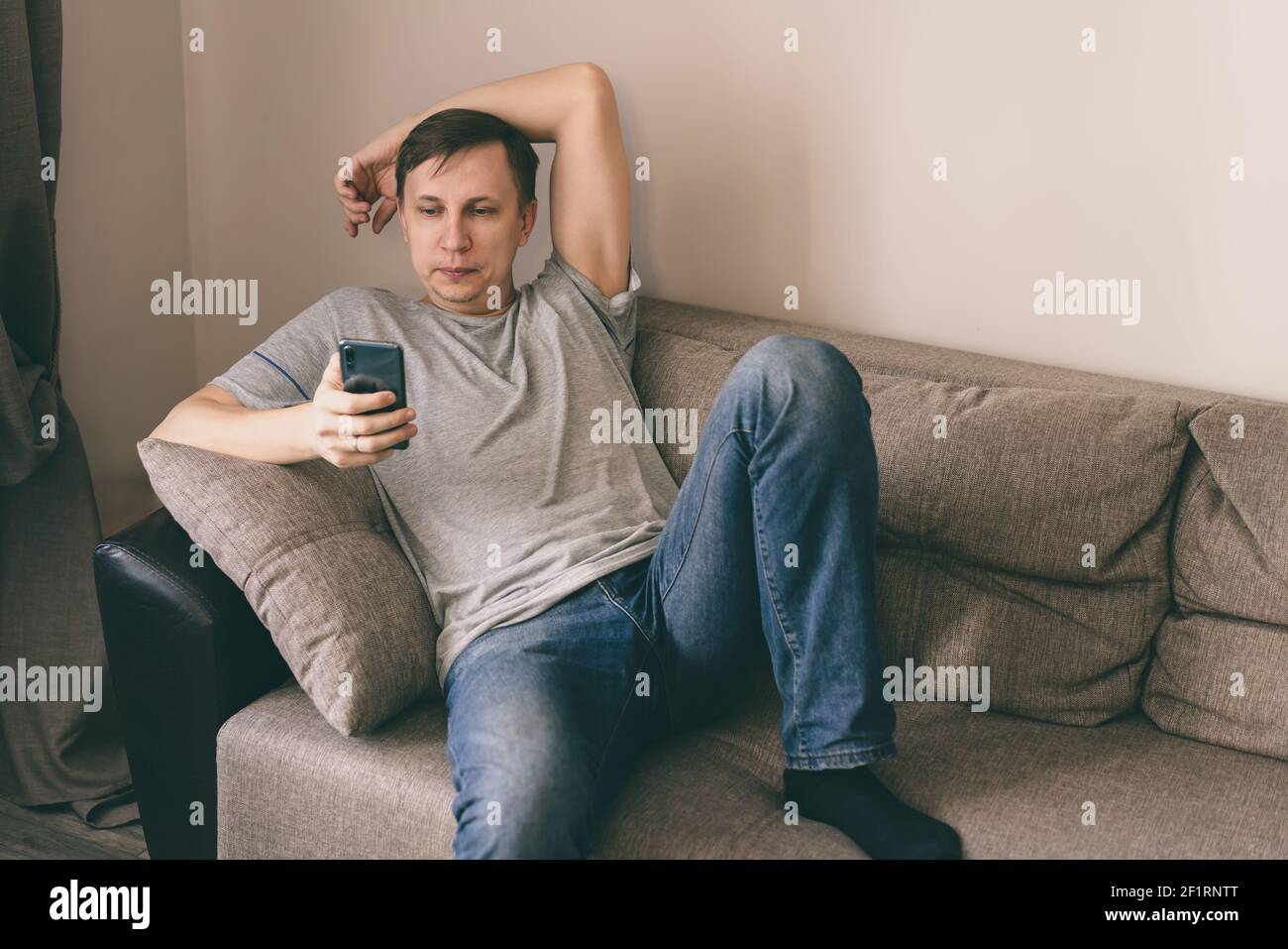 Serious man having rest using smartphone sitting on sofa at home Stock Photo