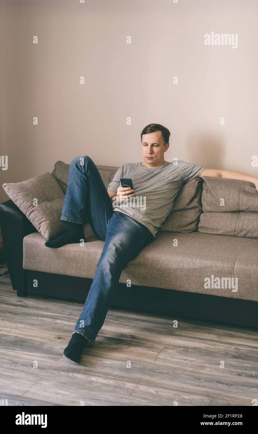 Serious man having rest using smartphone sitting on sofa at home Stock Photo