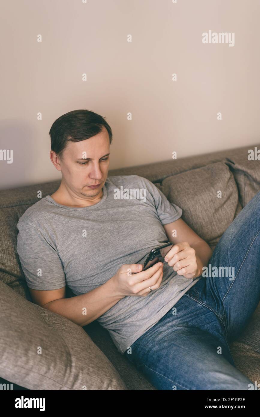 Serious man having rest using smartphone sitting on sofa at home Stock Photo