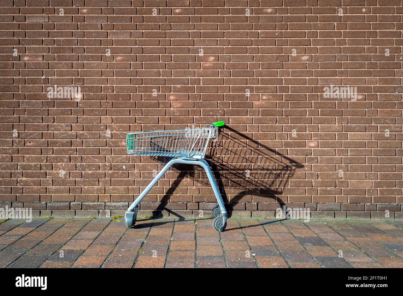 abandoned, empty supermarket trolley by a brick wall, shopping concept. Stock Photo