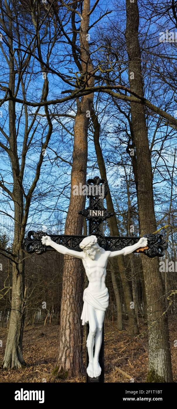 Cross and Jesus Christ statue on forest background. Religious symbol. Catholicism and Christianity concept.Monuments and statues in Europe. Cemetery Stock Photo