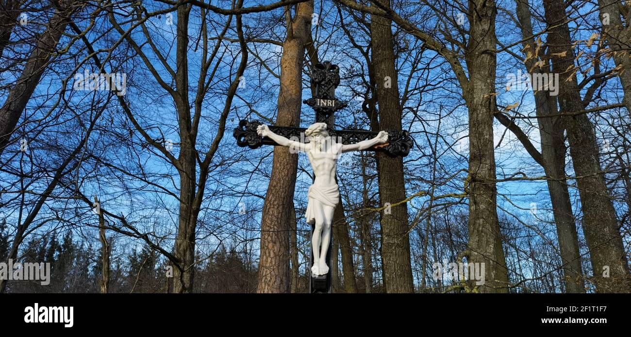 Cross and Jesus Christ statue on forest background. Religious symbol. Catholicism and Christianity concept.Monuments and statues in Europe. Cemetery Stock Photo