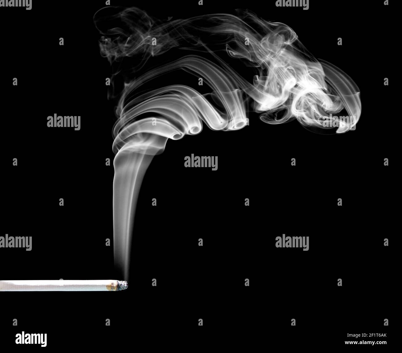 Close-up of a white smoke cloud coming from a lit slim cigarette against black background. Stock Photo