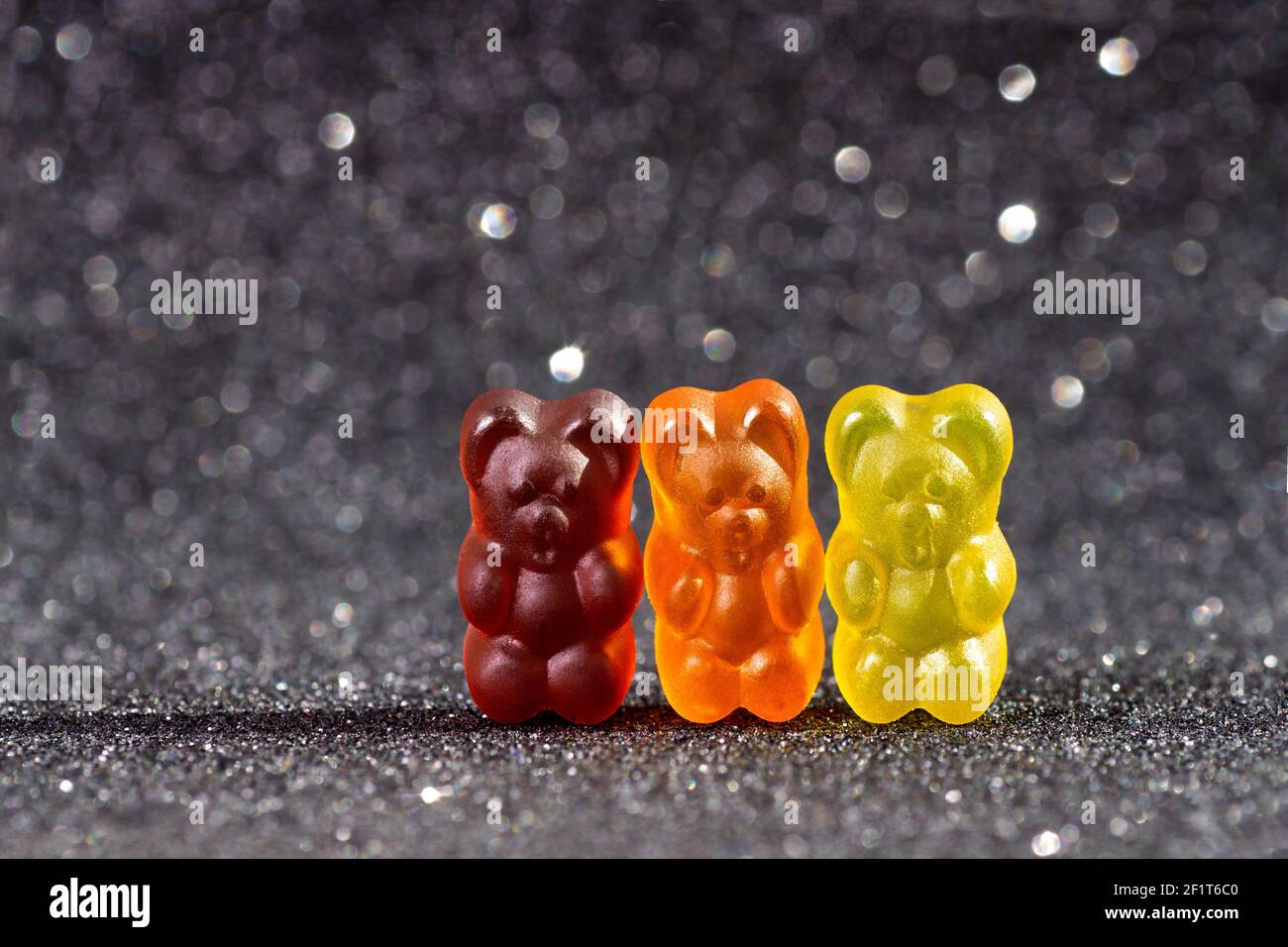 Close-up of three colored gummy bears standing against a black background Stock Photo