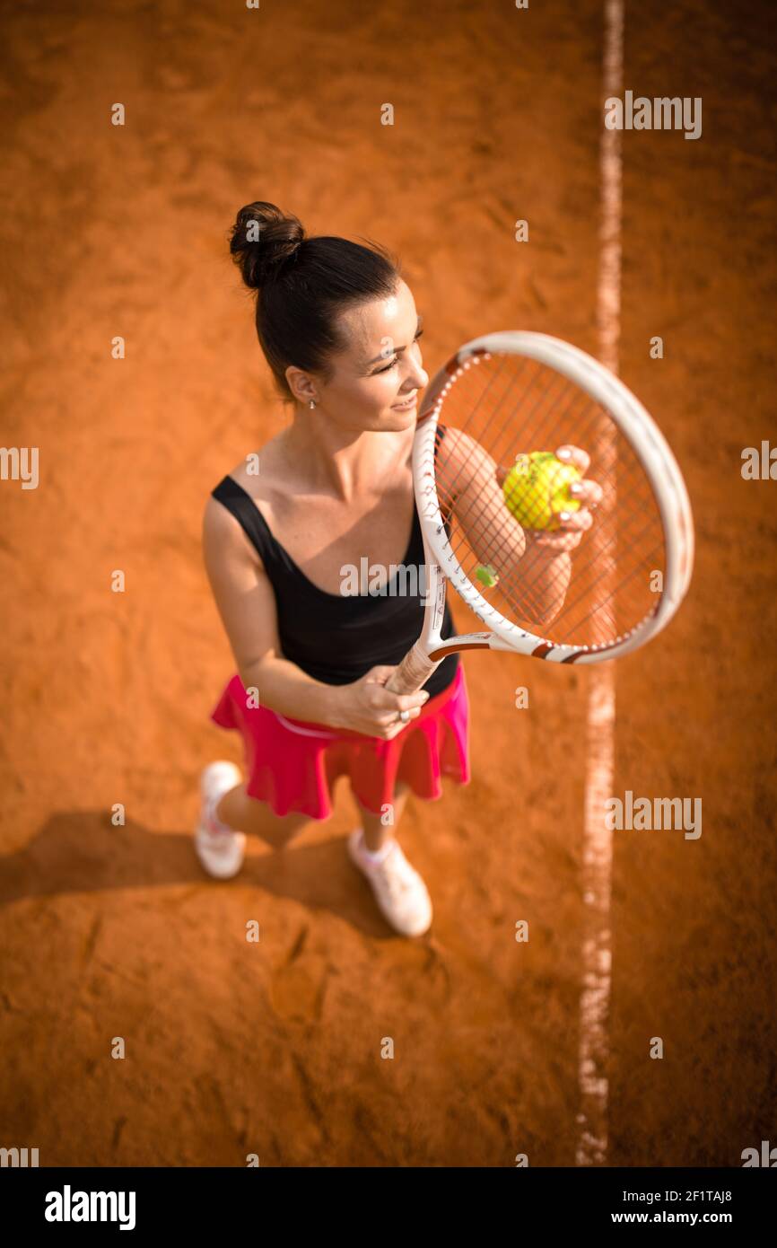 Top view of attractive young woman tennis player serving on a clay tennis court. Interesting POV
