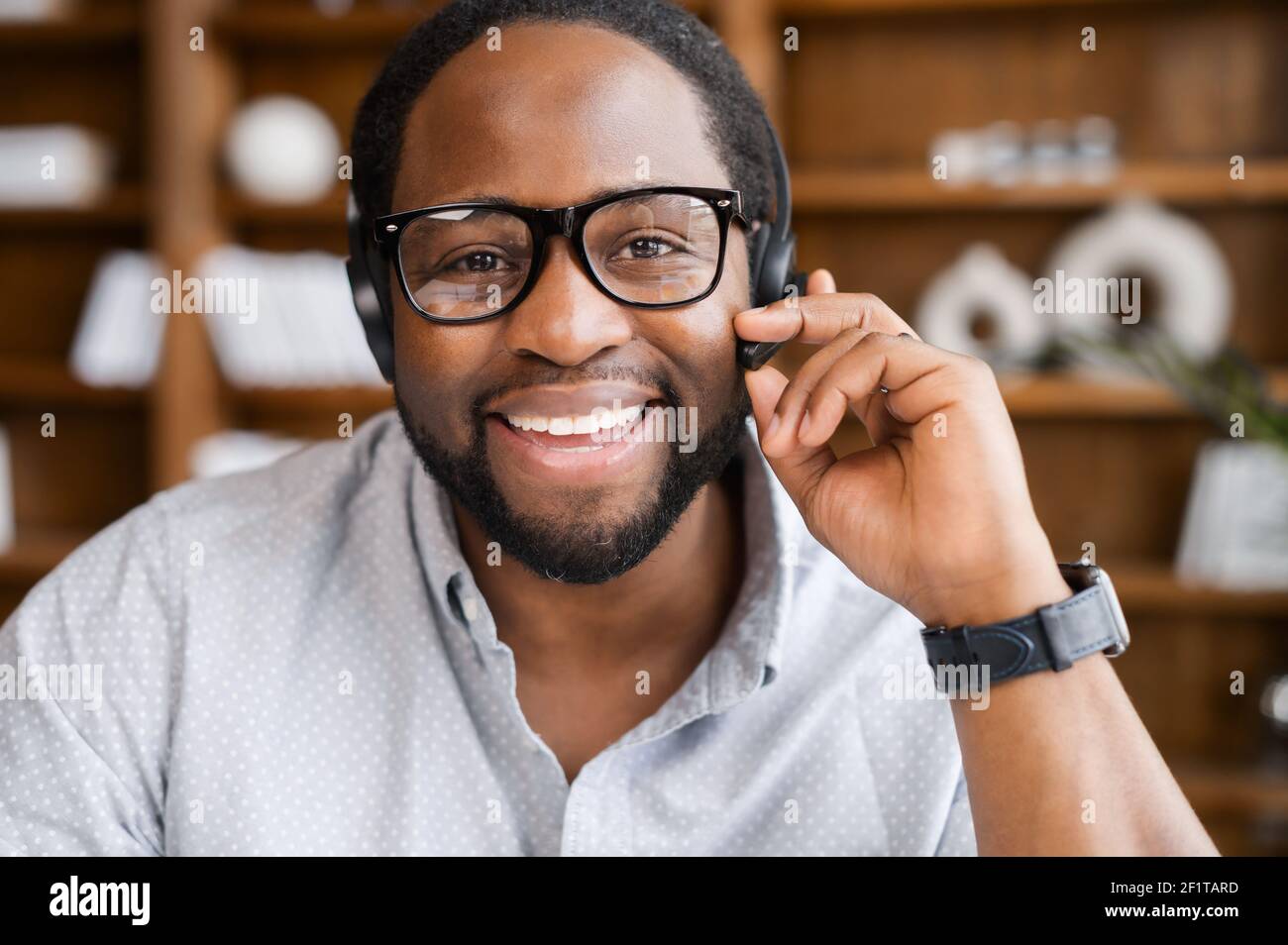 Webcam view of cheerful African American young businessman in a headset holding the microphone, attentive male customer service representative responding to the customer inquiry Stock Photo