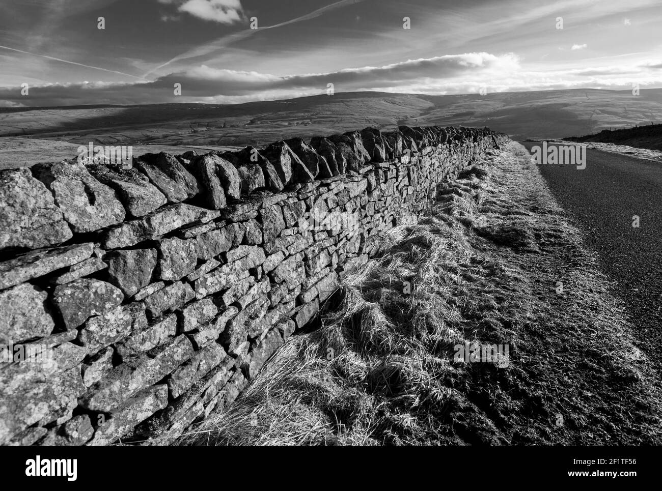 A dry stone wall in winter sunlight, leading into the distance alongside a country lane in the North Pennines, County Durham, England -B&W, monochrome Stock Photo
