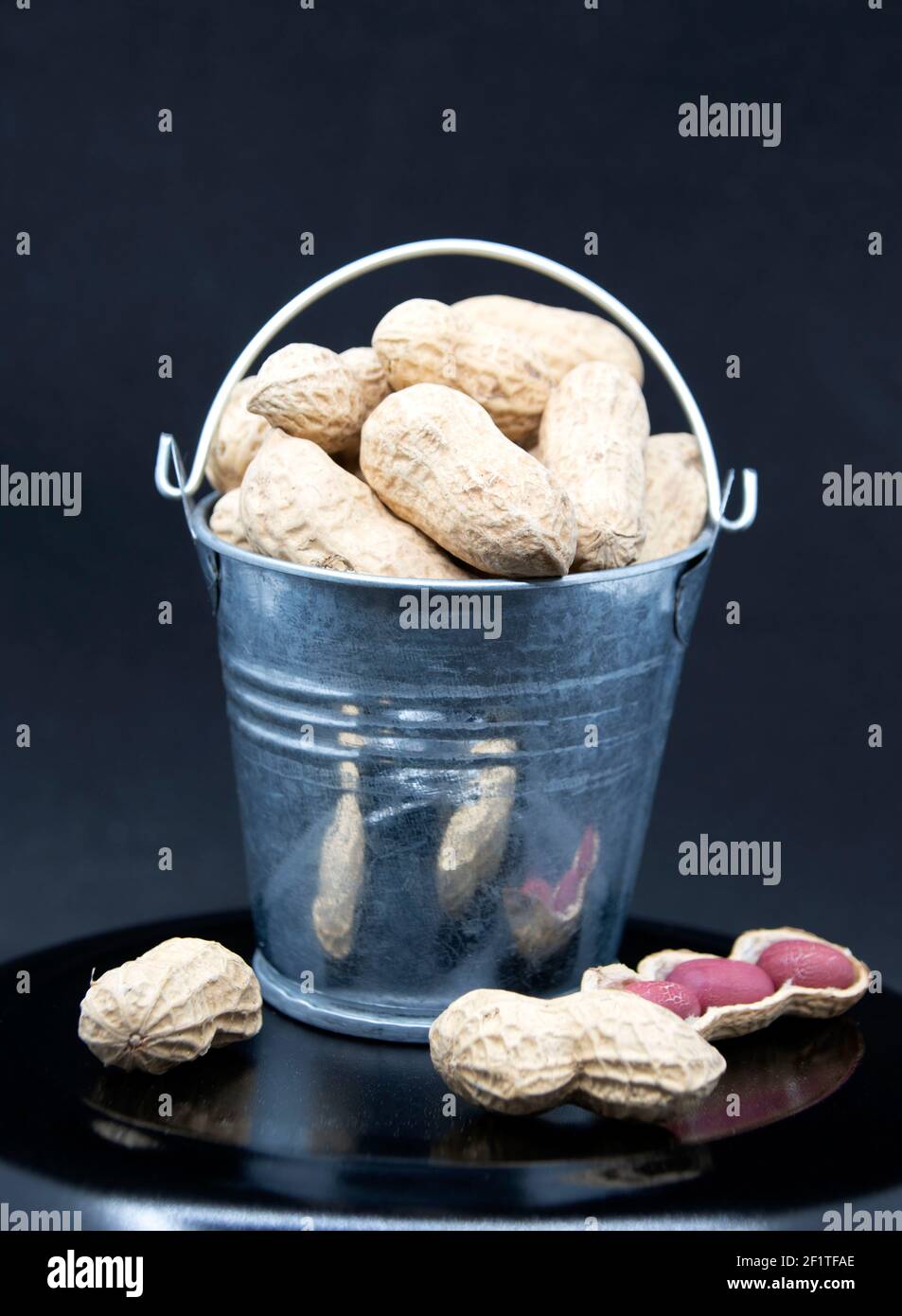 Red peanut seeds in miniature bucket on black background. Stock Photo