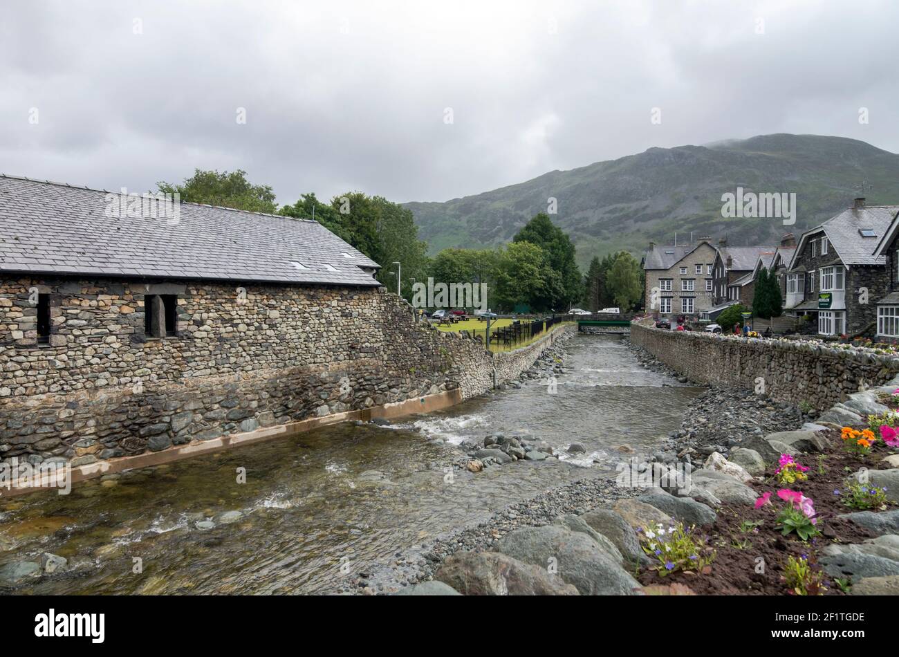 Glenridding Beck, runs through stone banks in the centre of the village.  The Ullswater Visitor Centre is on the left, Lake District, Cumbria. Stock Photo