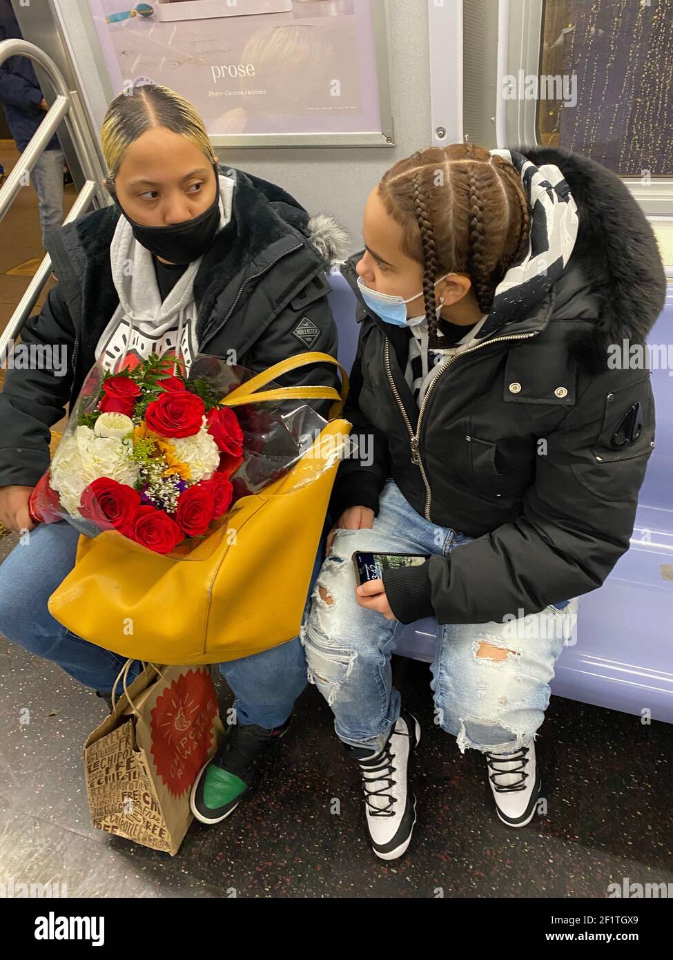 Mother and daughter with a bouquet of flowers ride a New York City subway train during the beginning of the 2nd year of the Covid-19 pandemic. Stock Photo