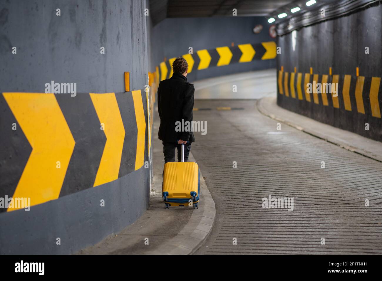 Man with a rolling suitcase in a parking. Man in a parking garage Stock Photo