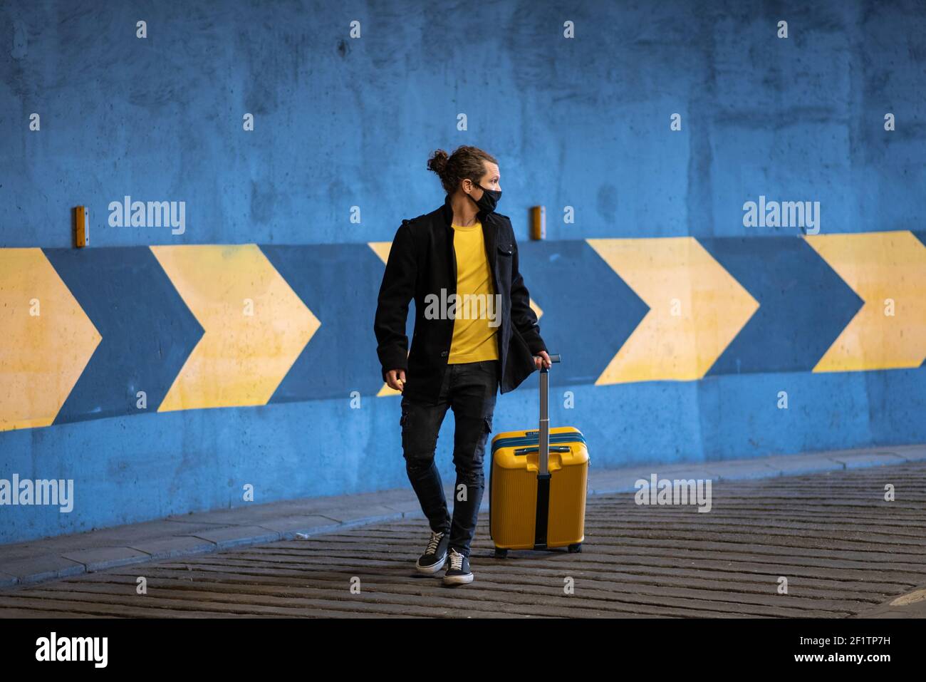 Man with a rolling suitcase in a parking. Travel during a pandemic Stock Photo