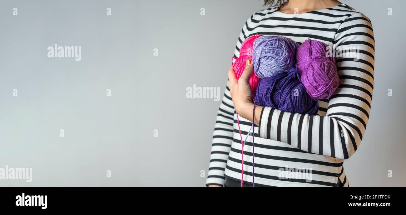 Woman with striped T-shirt and orange nail polish stacks in her arm some colorful balls of acrylic wool with copy space Stock Photo