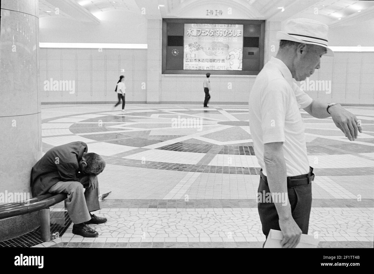 Man checking the time and homeless man sleeping on bench at train station in Tokyo, Japan. Stock Photo