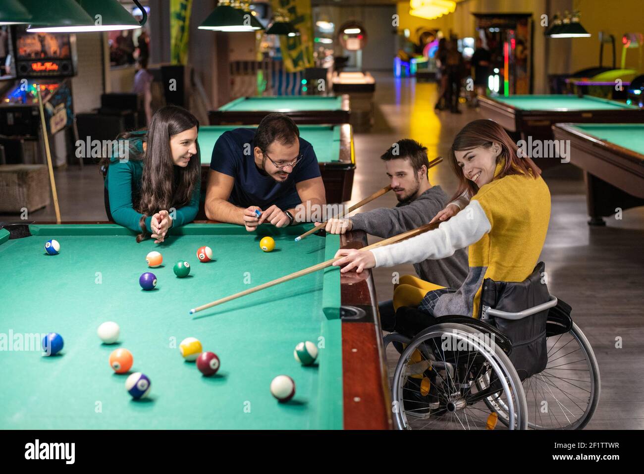Disabled girl in a wheelchair playing billiards with friends Stock Photo
