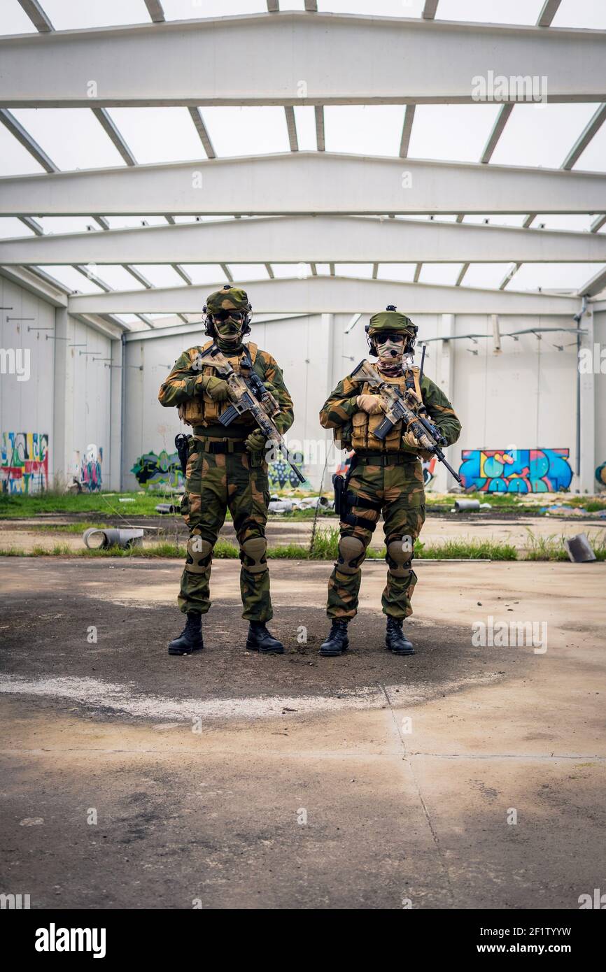 Two fully equipped soldiers posing with assault rifles in a covered area Stock Photo