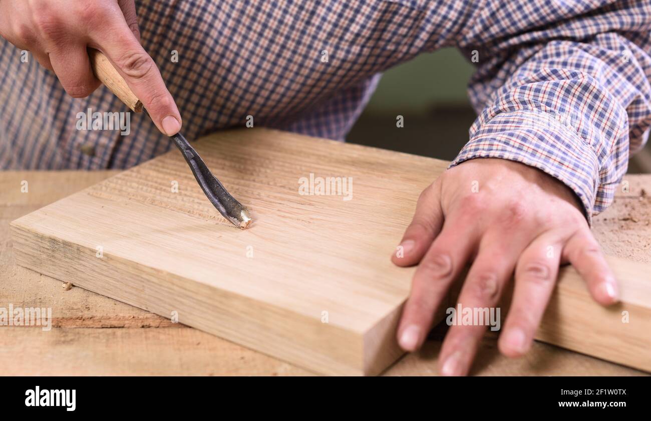 Carpenter hands working on wooden board with chisel closeup Stock Photo