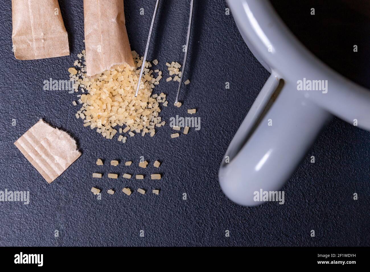 Sweetening tea with cane sugar. Arranged sugar grains on the table. Dark background. Stock Photo