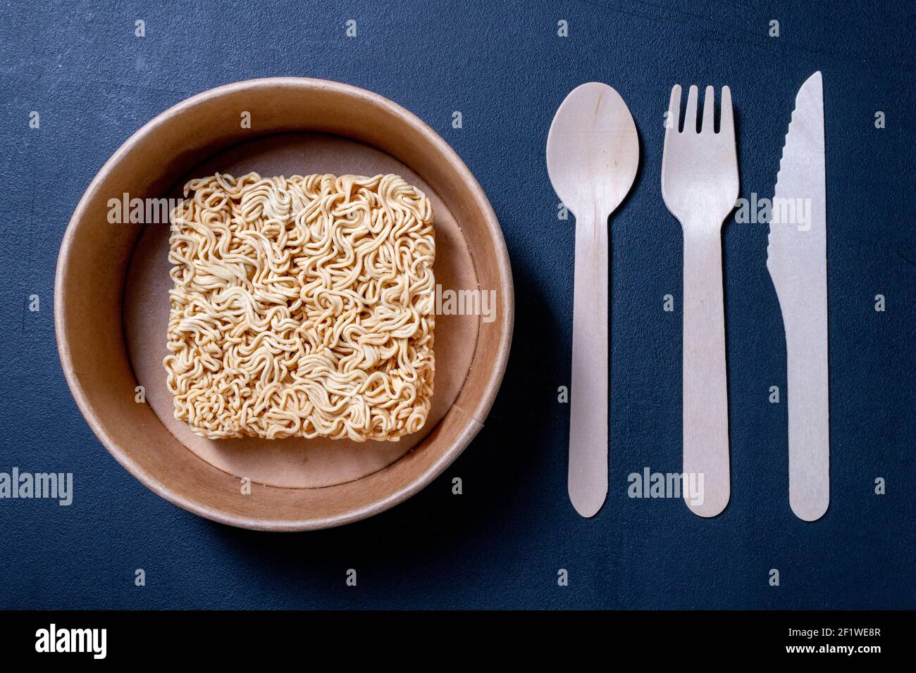 Chinese noodle soup on the kitchen table. Disposable wooden cutlery for eating instant meals. Dark background. Stock Photo