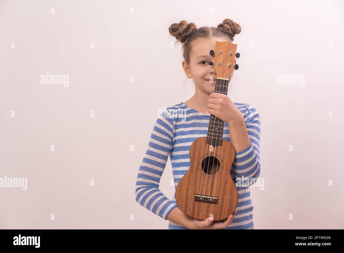 A child holds a ukulele in his hands. Small creative children. Girl learns to play an instrument online. Stock Photo