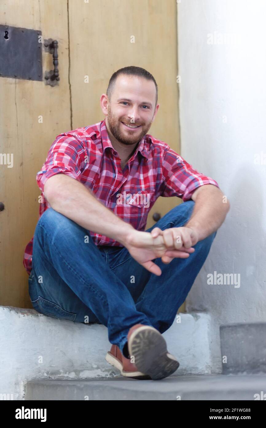 Young bearded man sitting at a door Stock Photo