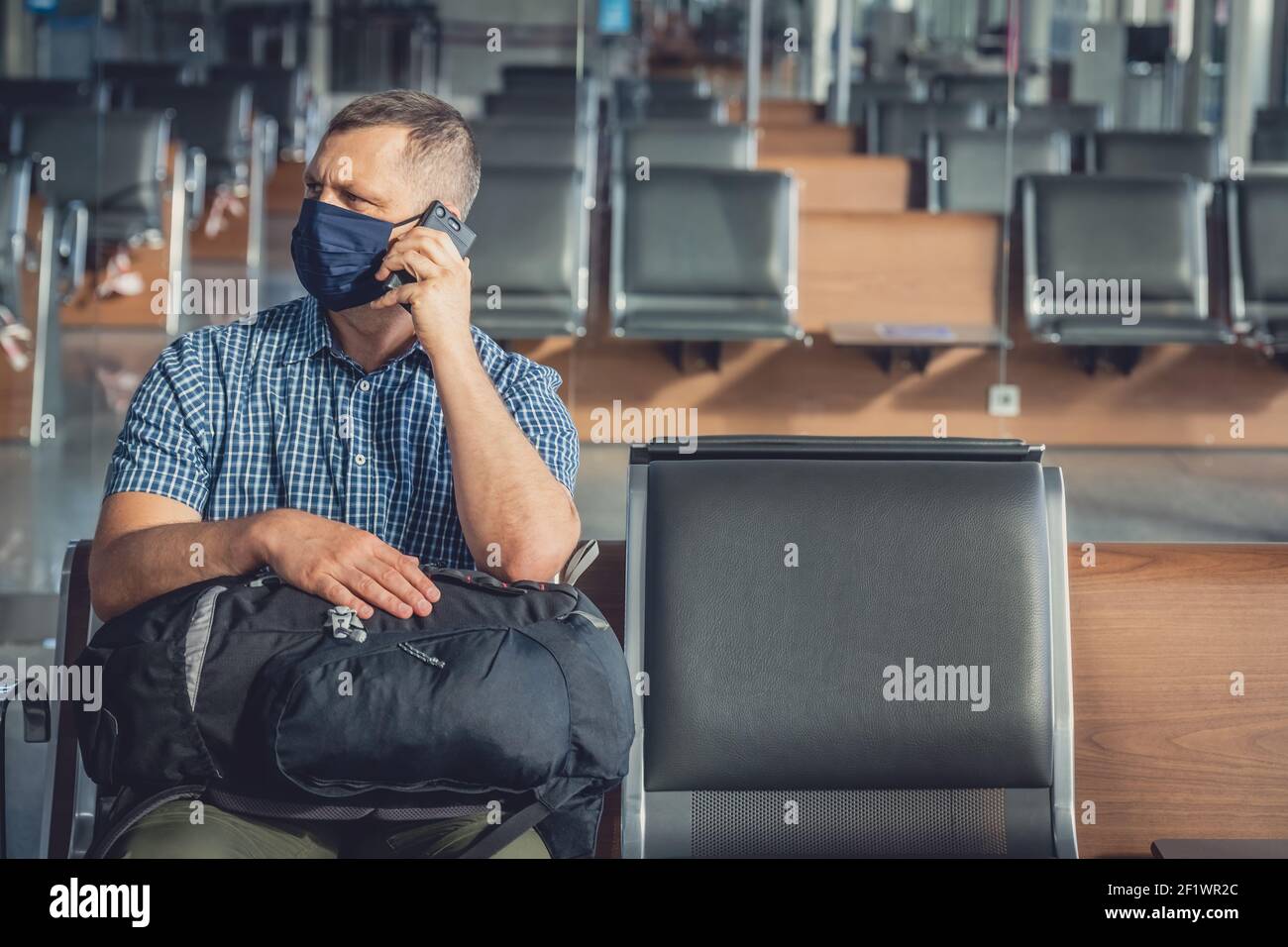 Man with a mask talking on mobile phone in airport lounge Stock Photo