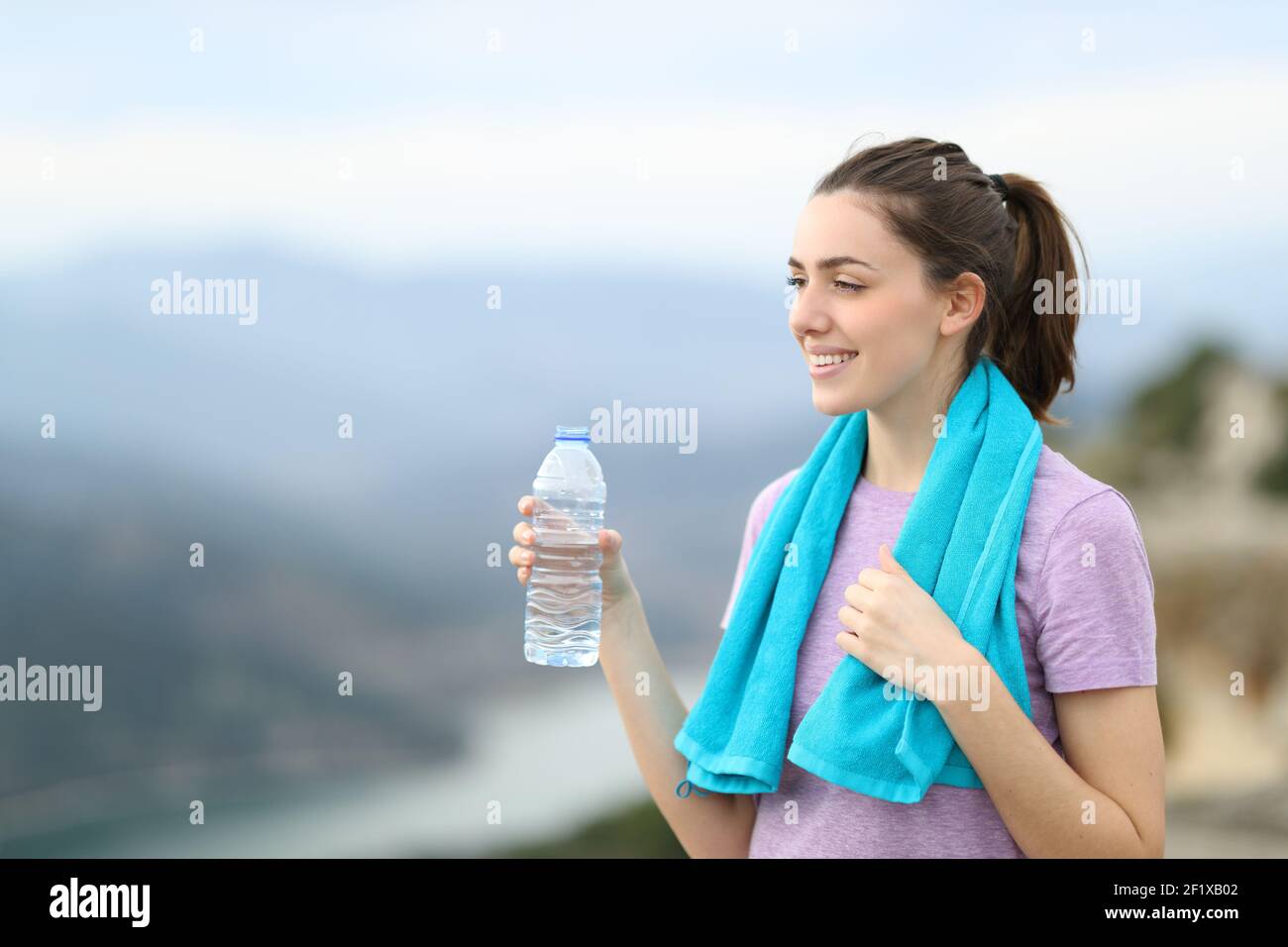 Happy jogger holding a bottle of water contemplating views after sport in the mountain Stock Photo