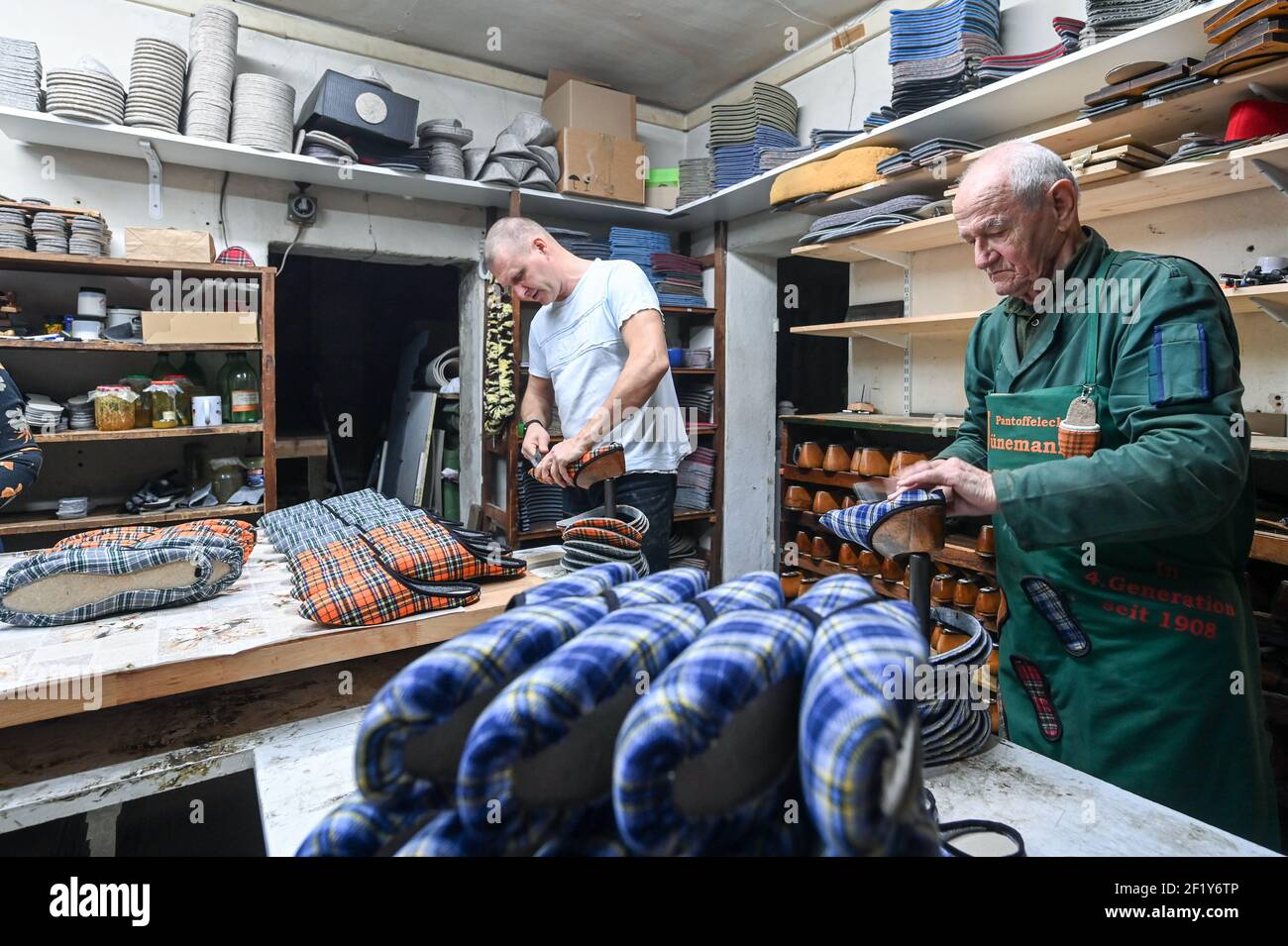 04 March 2021, Berlin: Owner Reno Jünemann (l) and his father, 82-year-old Günter Jünemann, use pincers to pull the fabric over lasts for the slipper into shape in the family business Jünemanns Pantoffeleck in Torstraße. Slippers have been produced here for over 100 years. Since 1992 the company is the last of its kind in Berlin. It is now run by the fourth generation. Slippers in all sizes and with different soles are produced by hand in 15 different colours and patterns. Currently there are a lot of online orders in the Corona pandemic. Photo: Jens Kalaene/dpa-Zentralbild/ZB Stock Photo