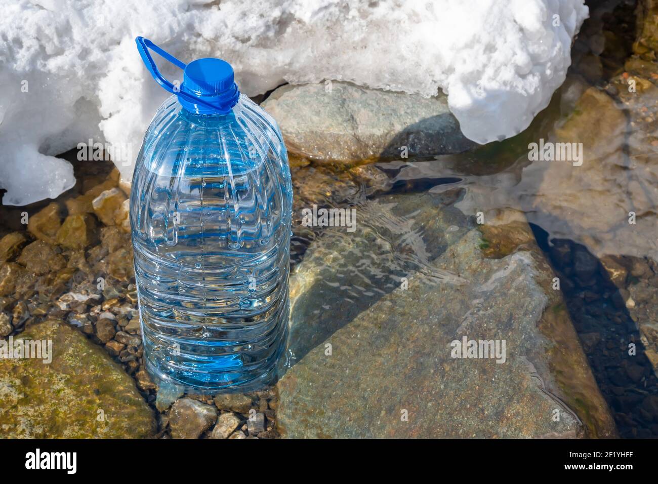 five liter plastic bottle filled with pure life-giving fresh water stands on the stone bottom of a spring, river, near the melting snow in the spring Stock Photo