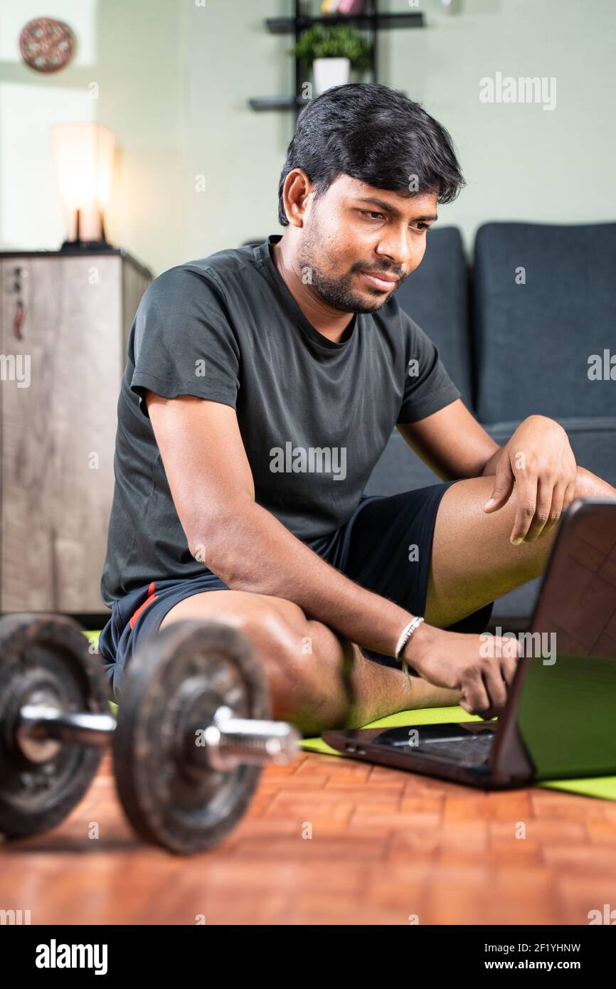 young man busy working on laptop during workout - Millennial searching or  waiting for online yoga class on mat - Concpet of new normal, work from home  Stock Photo - Alamy